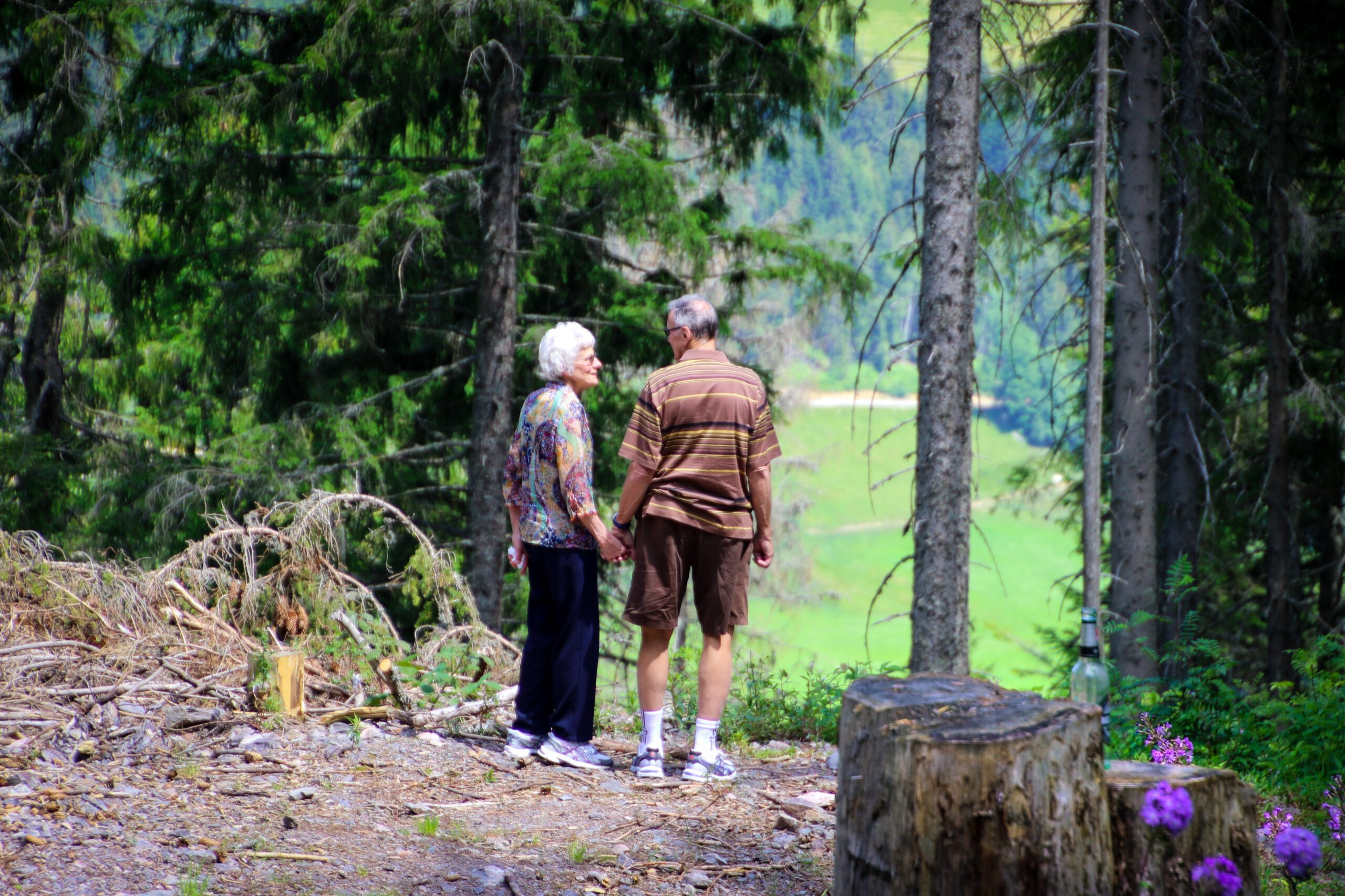 Starsza para trzymająca się za rękę i stojąca w lesie