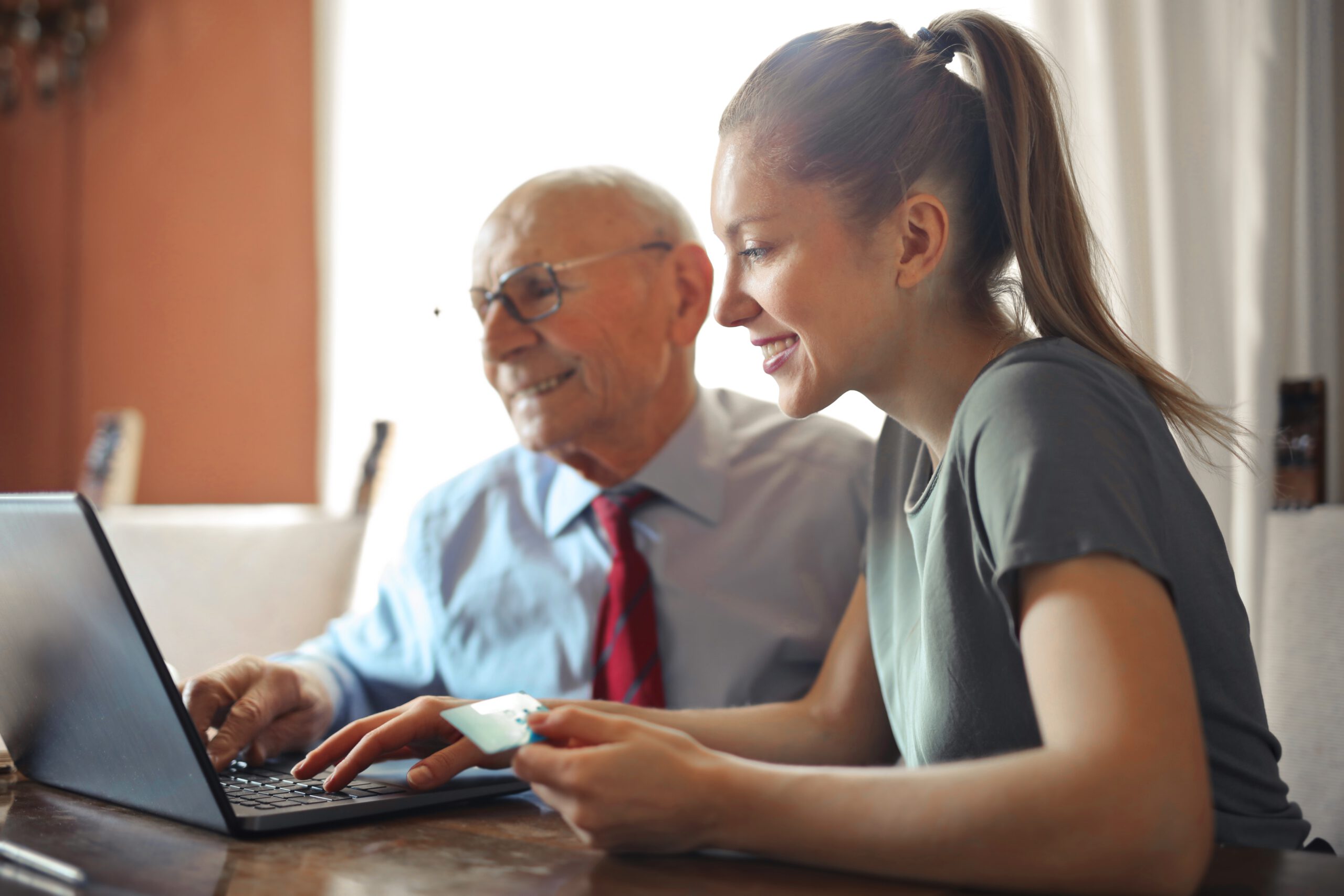 Starszy mężczyzna i jego opiekunka siedzący i uśmiechający się przed laptopem